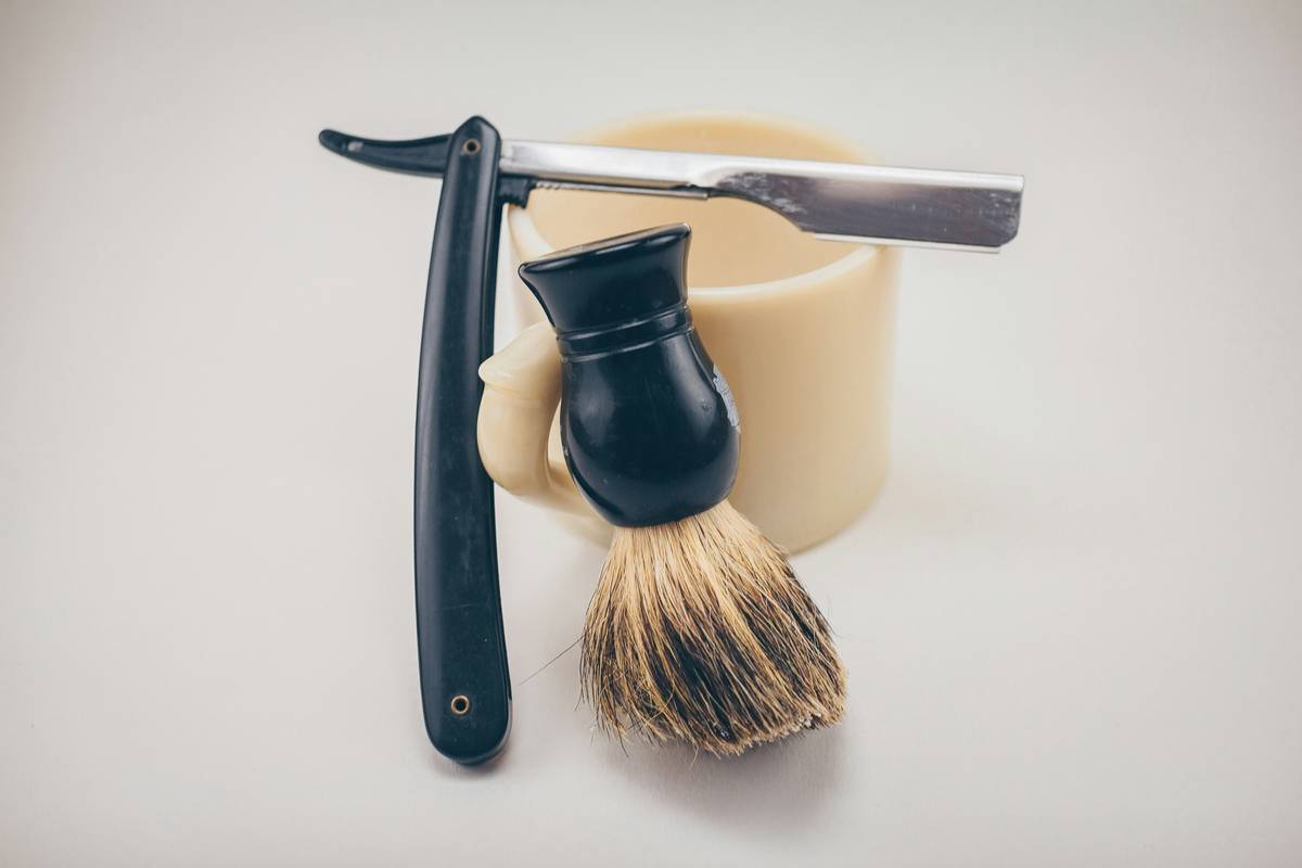 Close-up of grooming supplies beard oil blends beside a shaving brush and soap bowl